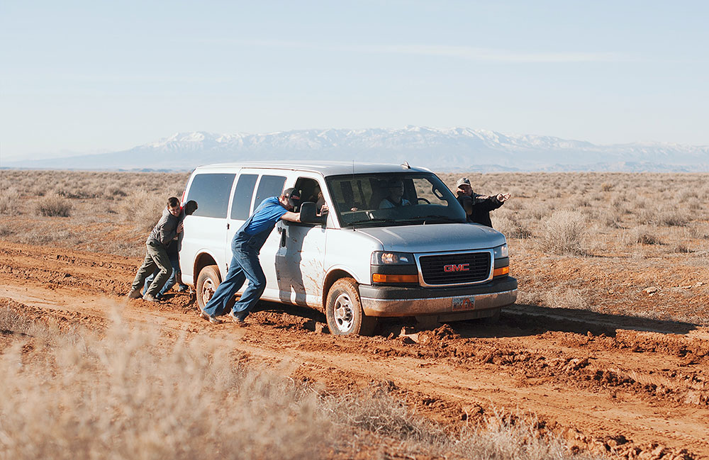 Mehrere Männer schieben in der Wüste einen Van.